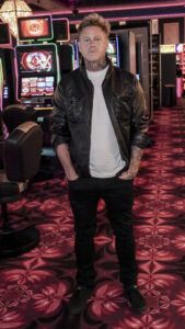 Muž v kožené bundě pózuje před hracími automaty v kasínu Vestec, v pozadí automaty